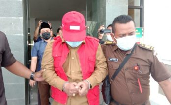 Camat Duduksampeyan, Gresik menutupi wajah dengan topi dari jepretan para wartawan di kantor kejaksaan negeri Gresik pada Senin, 15 Februari 2021