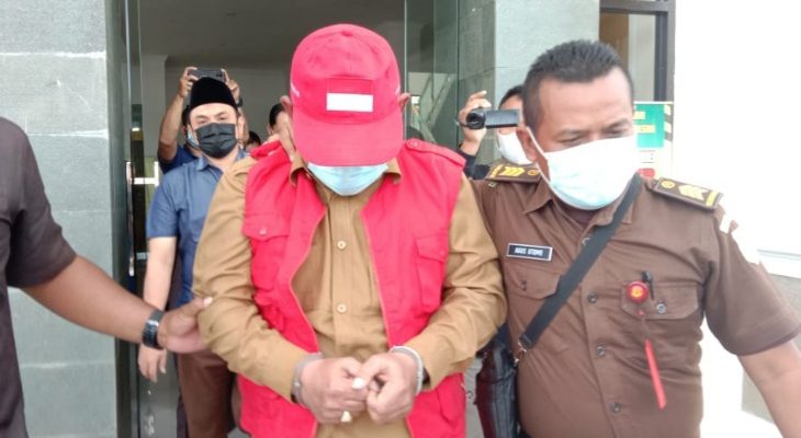 Camat Duduksampeyan, Gresik menutupi wajah dengan topi dari jepretan para wartawan di kantor kejaksaan negeri Gresik pada Senin, 15 Februari 2021