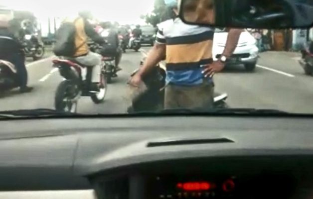 Seorang lelaki membawa paving menghentikan pengendara mobil di Jalan Raya Sukomulyo, Kecamatan Manyar, Gresik pada Jumat, 19 Februari 2021 (foto : screenshot video)